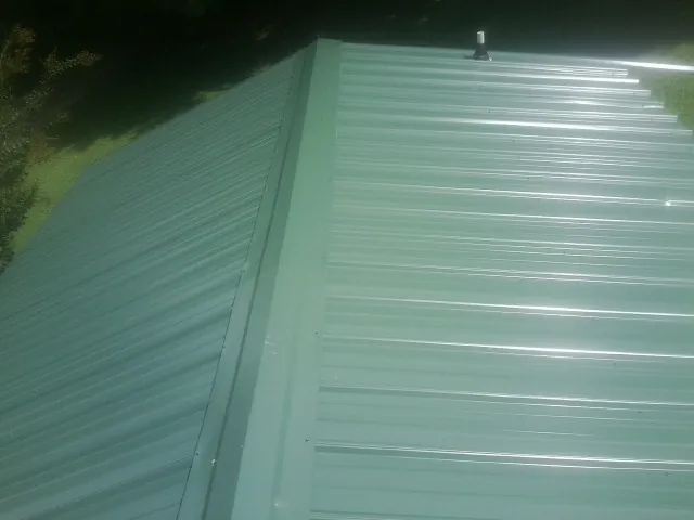 New green metal panels meeting at the ridge of a roof — Flat Roof Repair work by our crew in Gifford